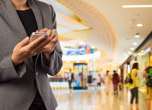 Verve News Articles Woman walking using mobile phone - shopping mall in background