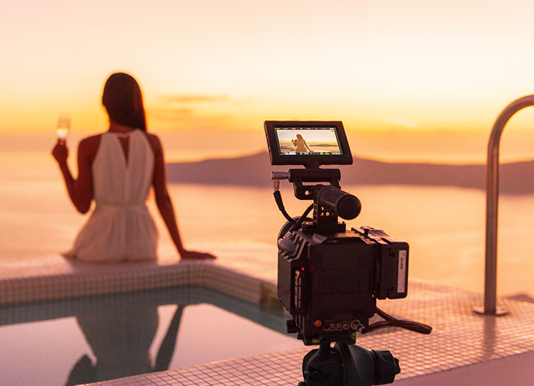 Lady sitting at the pool with a drink and camera filming her