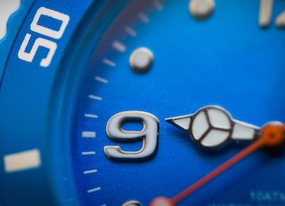 Close up of blue clock with hand on the 9